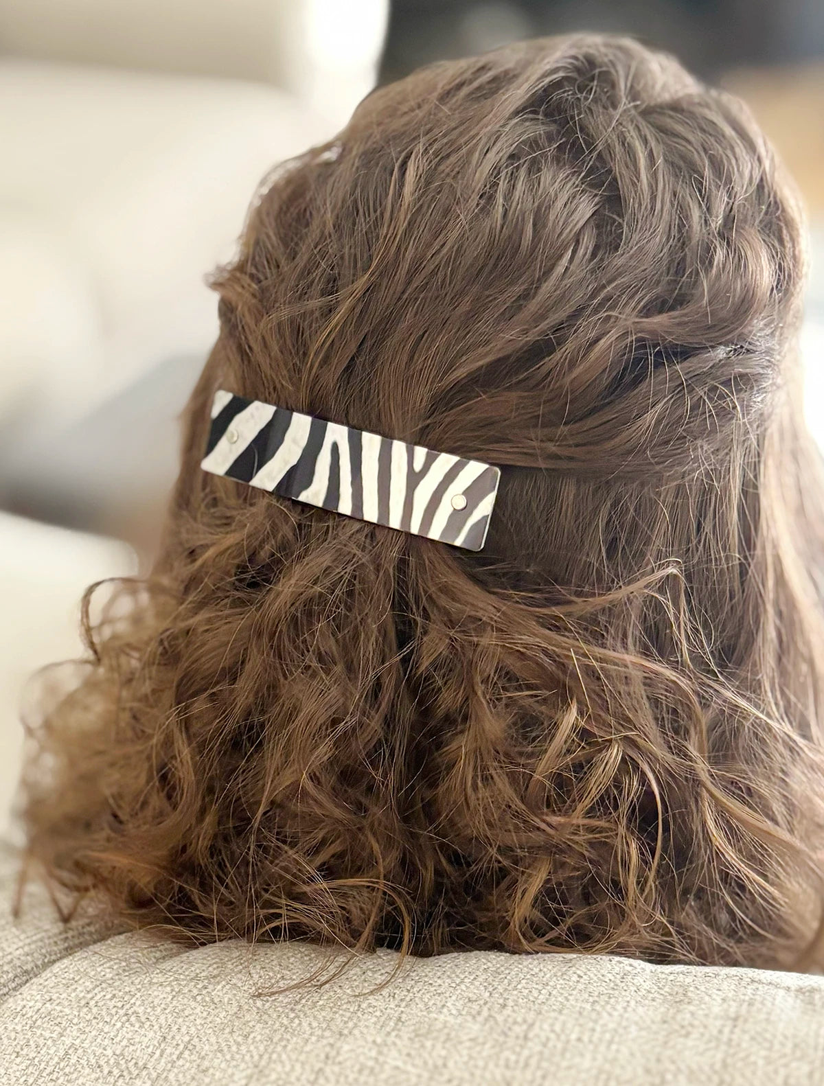 A close-up back view of a person with brown curly hair wearing a black and white zebra-print hair clip on the back of their head.