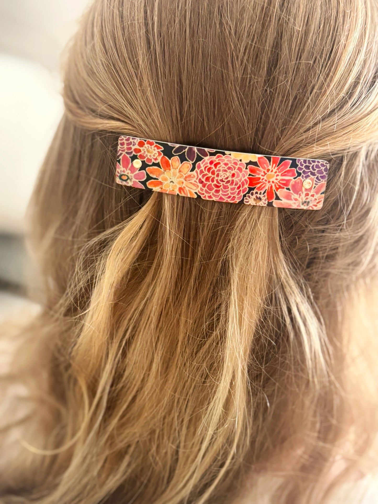 A close-up of a person's blonde hair secured with a rectangular hair clip featuring a colorful floral pattern in orange, pink, red, and purple.